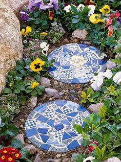 two blue and white mosaic stepping stones surrounded by flowers in a garden with large rocks