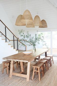 a dining room table with four stools and a plant in the center, under some hanging lights