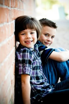 two young boys are leaning against a brick wall and posing for the camera with their arms around each other