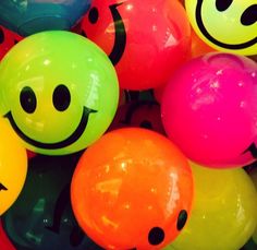 many different colored balls with smiley faces on them and one has a black face in the middle