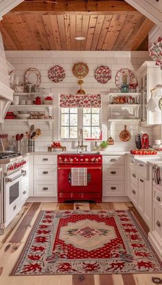 a red stove top oven sitting inside of a kitchen next to white cabinets and drawers