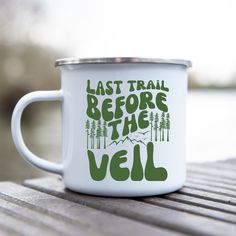 a white enamel mug with the words last trail before the veil on it sitting on a wooden table