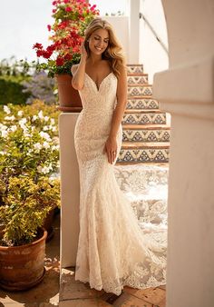 a woman in a wedding dress standing on some steps with flowers and potted plants behind her