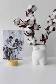 a white vase filled with cotton sitting next to a photo