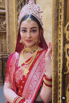 a woman in a red and gold sari is posing for the camera with her hands together