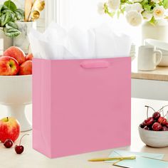 a pink shopping bag sitting on top of a table next to some apples and a bowl of cherries