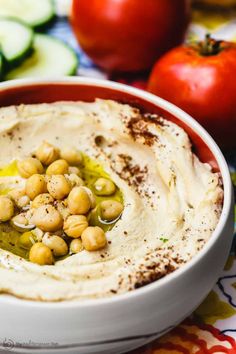 a white bowl filled with hummus and garnish next to sliced cucumbers