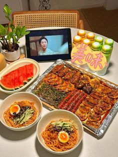 a table topped with plates and bowls filled with food next to a laptop computer on top of a table