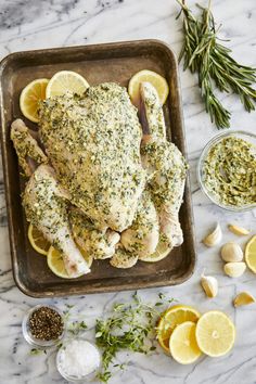 chicken with herbs and lemons on a baking sheet next to garlic, seasoning, salt and pepper