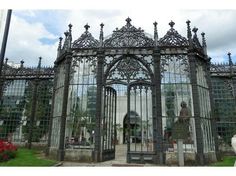 an ornate iron gate in front of a glass building with statues on the outside and inside