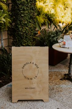 a wooden sign sitting on top of a cement ground next to a potted plant