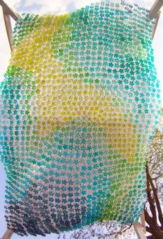 a sculpture made out of plastic beads on top of a wooden pole with trees in the background