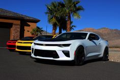 three different colored cars parked next to each other in front of a house with palm trees