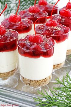 small desserts with cherries and whipped cream are on a tray next to pine branches