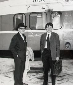 two men in suits and ties standing next to a train car with the name sabena on it