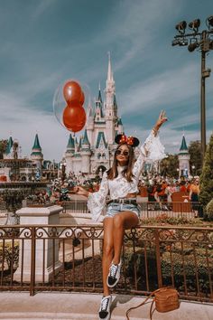 a woman sitting on top of a metal fence next to a red balloon in front of a castle