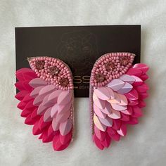 a pair of pink and red wings on top of a white sheet with a black card