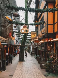 an alley way with christmas lights and decorations on the trees in front of buildings, people are walking down the street