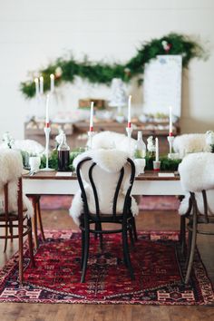 a dining room table with white fur chairs and candles on top of the wooden table