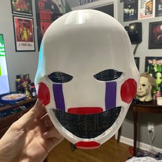 a person holding up a white mask with red and purple stripes