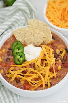 a white bowl filled with chili, cheese and tortilla chips on top of a table