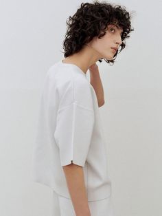 a woman with curly hair is wearing a white top and pants, looking off to the side