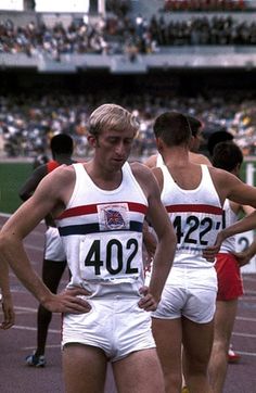 two men standing next to each other on a track with spectators in the stands behind them