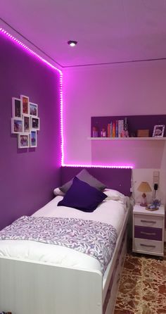 a bed room with a neatly made bed and purple lights on the wall above it