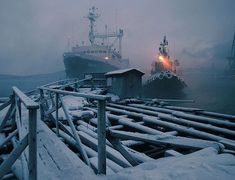 two boats in the water near a dock covered in snow and ice with lights on