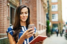 a woman looking at her cell phone while holding a book