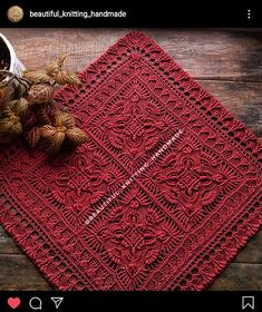 a red crocheted placemat sitting on top of a wooden table next to a plant