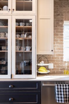 a kitchen with white cabinets and black counter tops next to a brick wall in the background