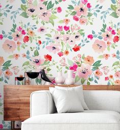 a white couch sitting in front of a wall covered in pink and green flowers on it