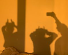 the shadow of a person holding a camera in front of a yellow wall and window