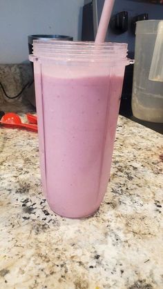 a pink smoothie in a plastic cup with a straw on the side sitting on a counter