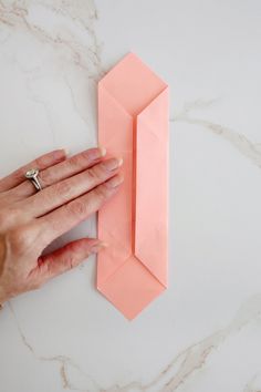 a woman's hand is holding the edge of an origami tie on a marble surface