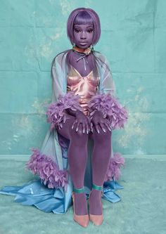 a doll with purple hair sitting on top of a blue sheeted floor next to a wall