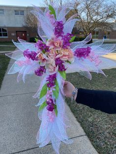 a person holding a cross with purple flowers on it in front of a brick building