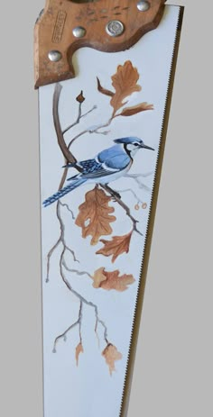 a blue bird sitting on top of a tree branch with leaves painted on it's side