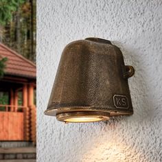 an old bell light on the side of a building next to a wall with a house in the background