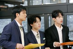 three young men in suits standing next to each other holding papers and looking at something