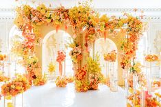 a white table topped with lots of orange and yellow flowers next to tall pillars filled with candles