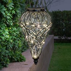 A Tear Shaped Solar Glass hanging lantern framed by a beautiful metal design makes an elegant statement! A glow will automatically illuminate from within as the 15 Solar powered warm white LED firefly lights begin to glow at dusk. Hang anywhere in your garden you want a dazzling touch! Exhart 7-in x 24-in Clear Metal Solar Outdoor Decorative Lantern | 13173-RS Solar Hanging Lanterns, Firefly Lights, Curtain String Lights, Outdoor Hanging Lanterns, Lantern Lamp, Solar Lanterns, Glass Lantern, Solar Lights Garden, Patio Lighting