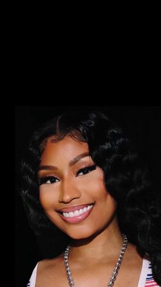 a close up of a person wearing a necklace and smiling at the camera with dark background