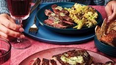 a person is eating steak and broccoli at a table with two glasses of wine