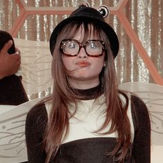 a woman wearing glasses and a hat making a funny face