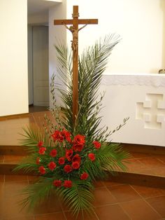 a crucifix with red flowers and greenery on the floor in front of it