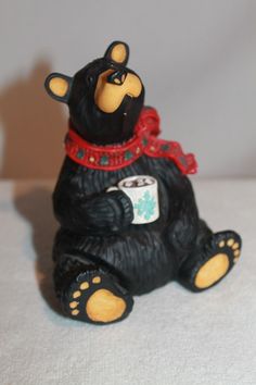 a black bear figurine with a red scarf around it's neck sitting on a white surface