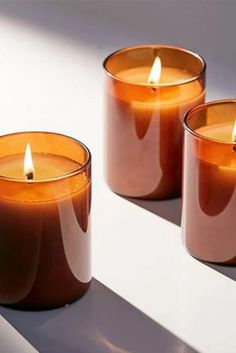 three candles sitting next to each other on top of a white surface with shadows from them