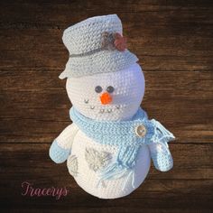 a crocheted snowman wearing a blue hat and scarf on top of a wooden table